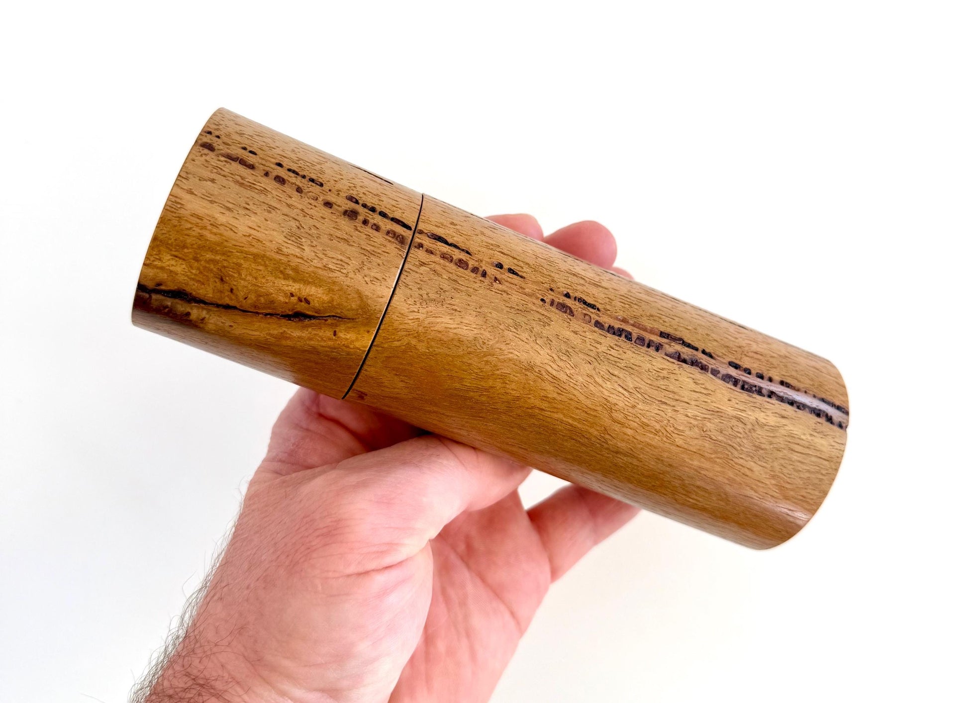 Mans hand holding single straight cylindrical Marri timber grinder