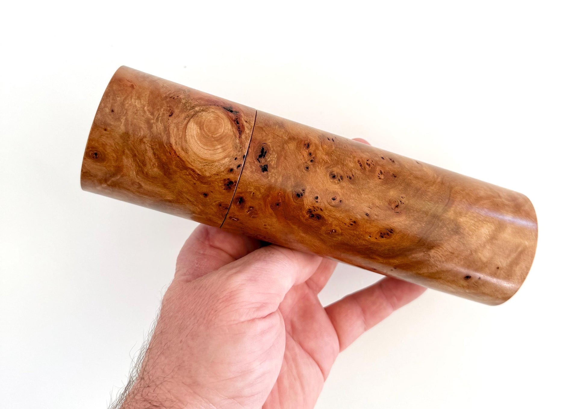 Mans hand holding single straight cylindrical Myrtle Burl timber grinder