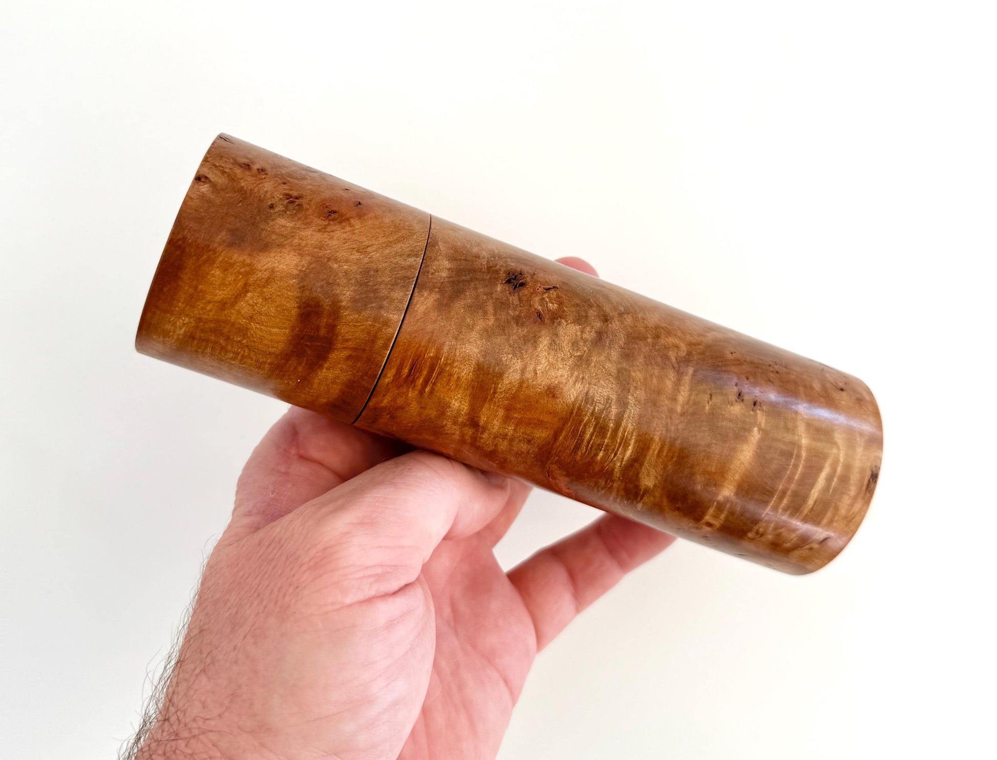 Mans hand holding single straight cylindrical Myrtle Burl timber grinder