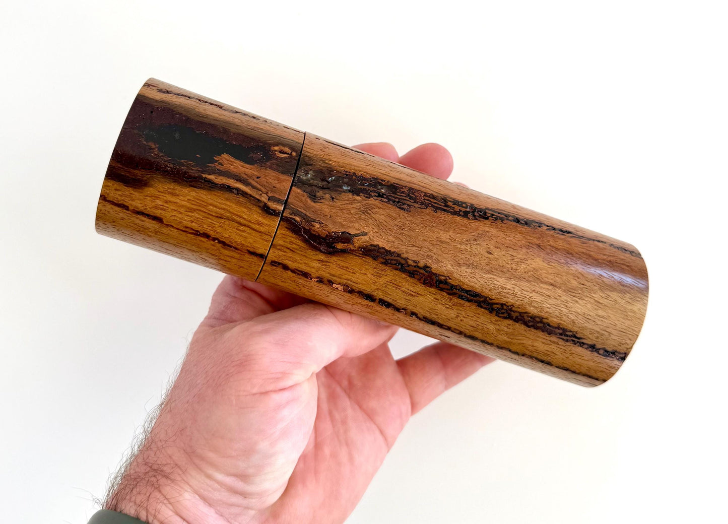 Mans hand holding single straight cylindrical Marri timber grinder