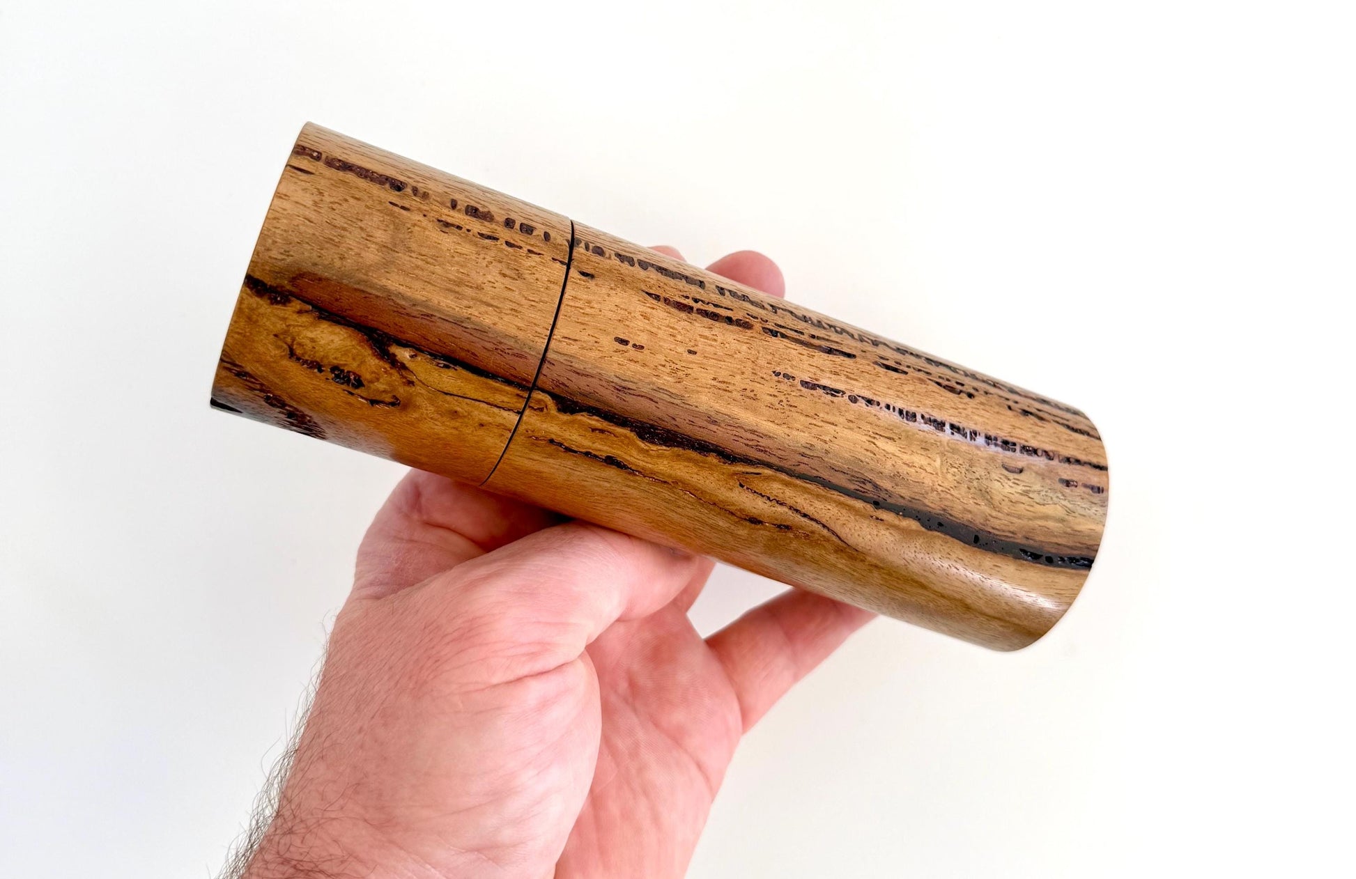 Mans hand holding single straight cylindrical Marri timber grinder