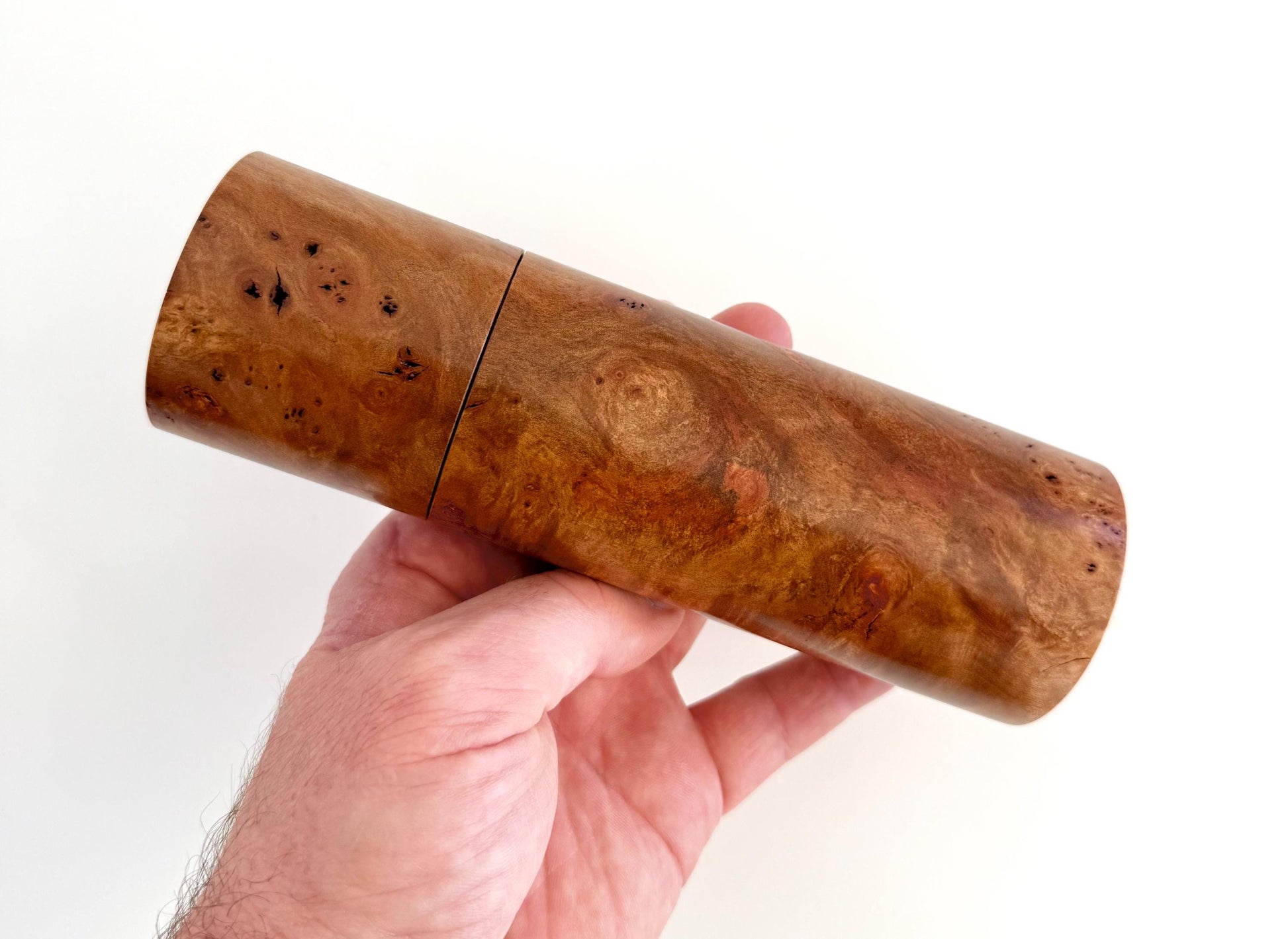 Mans hand holding single straight cylindrical Myrtle Burl timber grinder