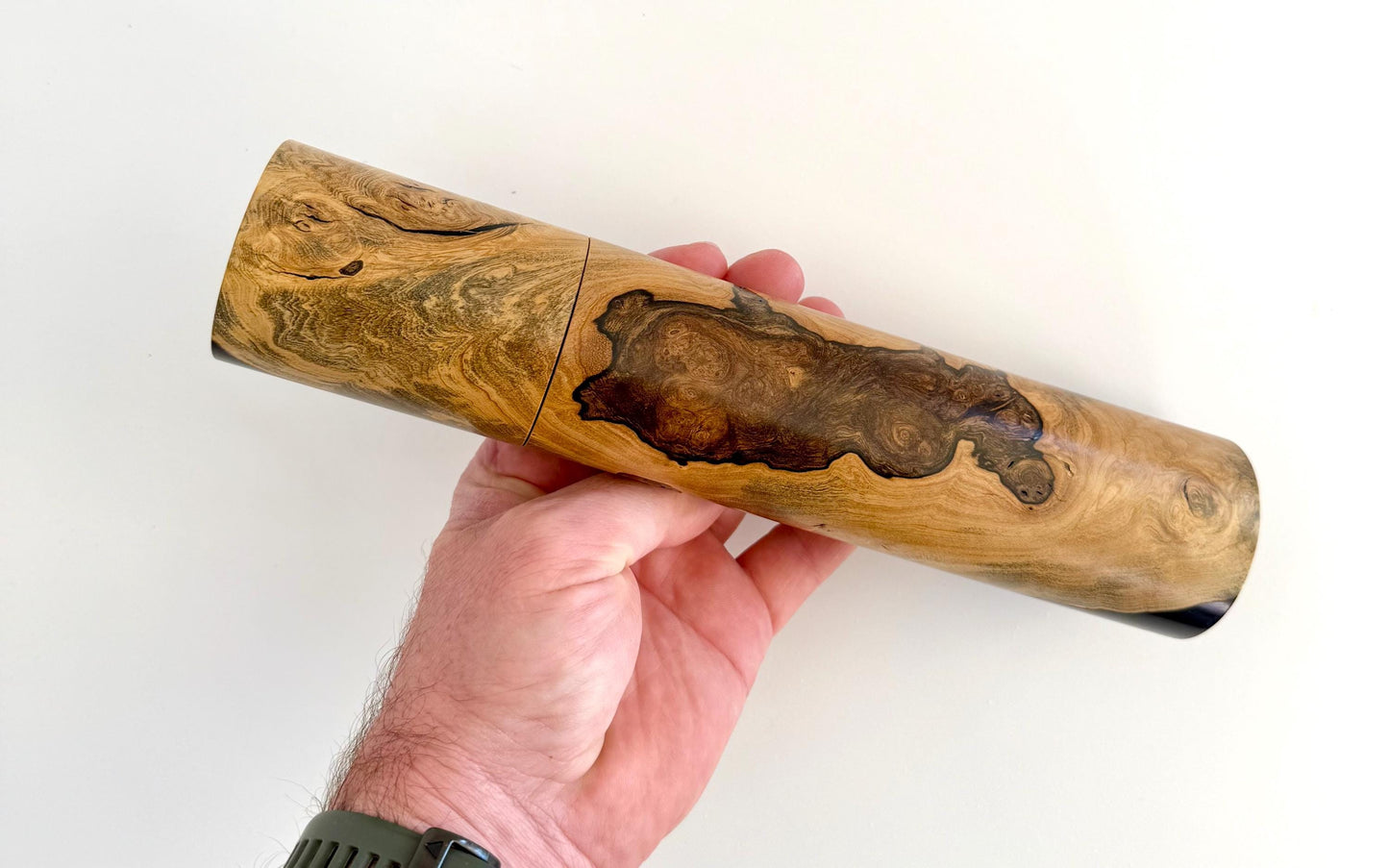 Mans hand holding single straight cylindrical Marri timber grinder