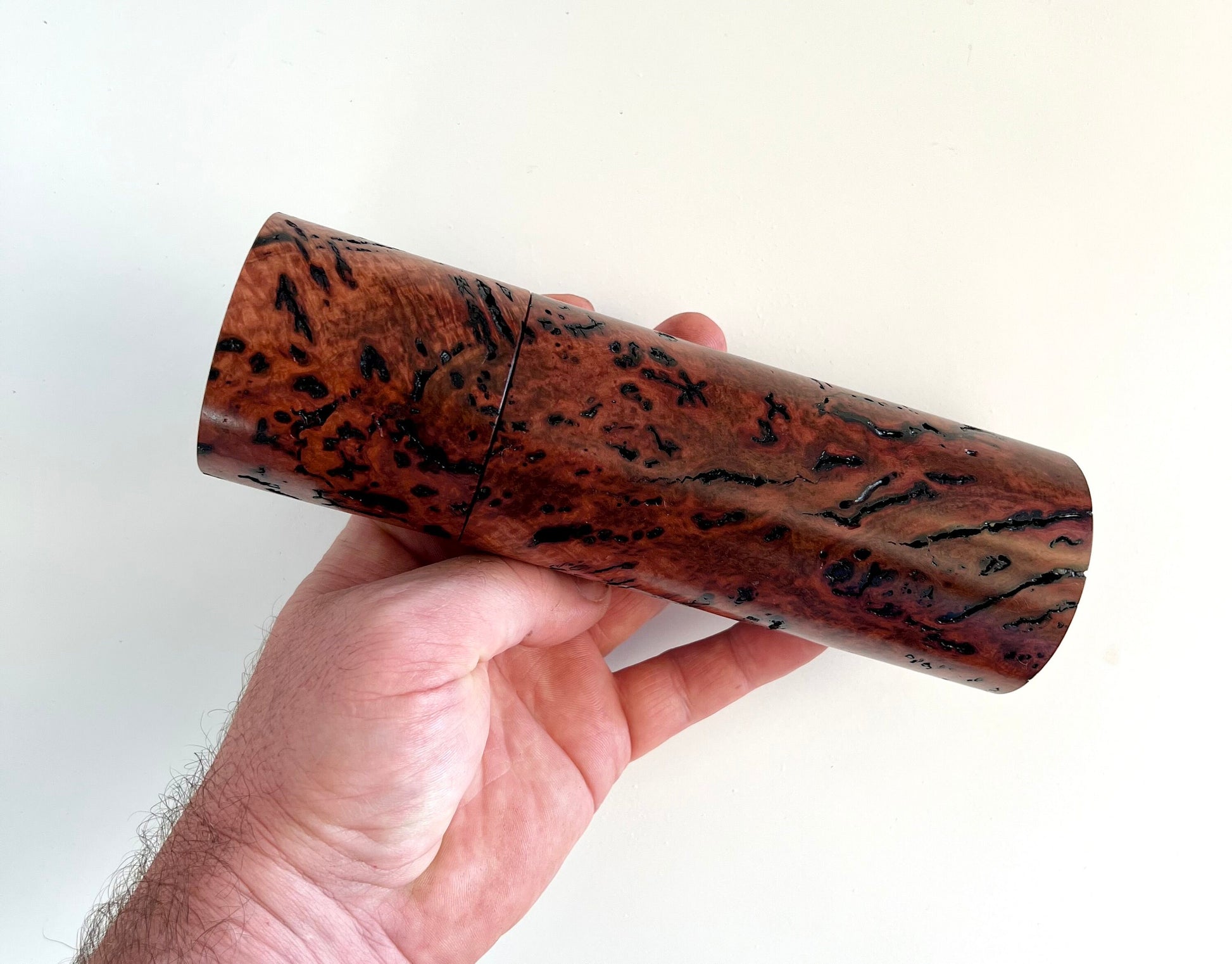 Mans hand holding single straight cylindrical salmon gum burl grinder